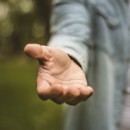 Help is always welcome. Young man in standing in park stretches his hand. Focus is on hand. Close up.