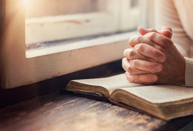 Hands of an unrecognizable woman with Bible praying