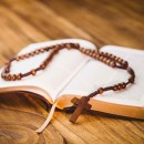 Open bible with rosary beads on wooden table