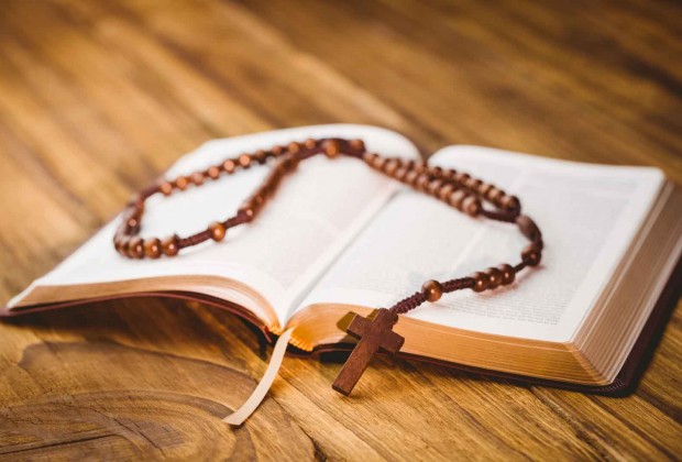 Open bible with rosary beads on wooden table