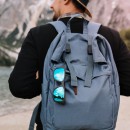 Outdoor portrait from back of male tourist carrying big decorated backpack and walking to mountains in morning. Man wearing black sweatshirt and brown hat travelling around Italy enjoys river view.