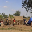 People standing outside of make shift shelters.  Over 25,000 internally displaced people are stranded in Metuge, a town in Cabo Delgado Province, northern Mozambique.