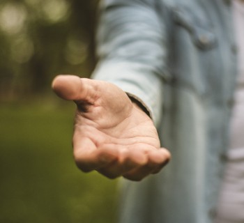 Help is always welcome. Young man in standing in park stretches his hand. Focus is on hand. Close up.