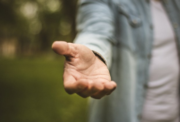 Help is always welcome. Young man in standing in park stretches his hand. Focus is on hand. Close up.