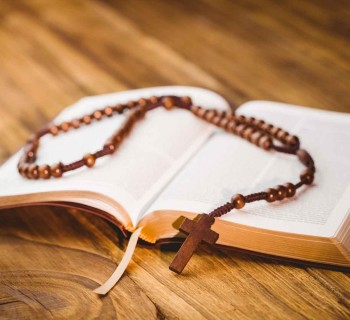 Open bible with rosary beads on wooden table