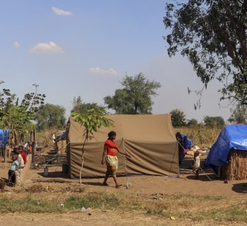 People standing outside of make shift shelters.  Over 25,000 internally displaced people are stranded in Metuge, a town in Cabo Delgado Province, northern Mozambique.